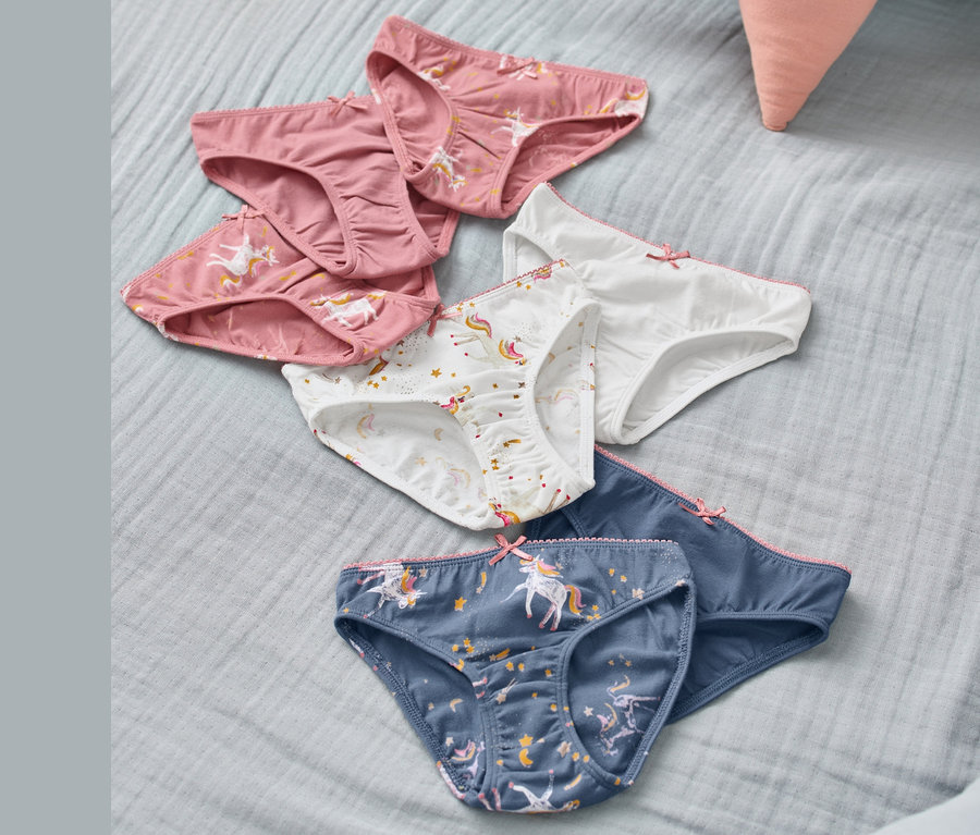 Na jasnoniebieskim materiale leżą figi dziewczęce, 7 par, w kolorach różowym, białym i niebieskim, z nadrukiem jednorożców.