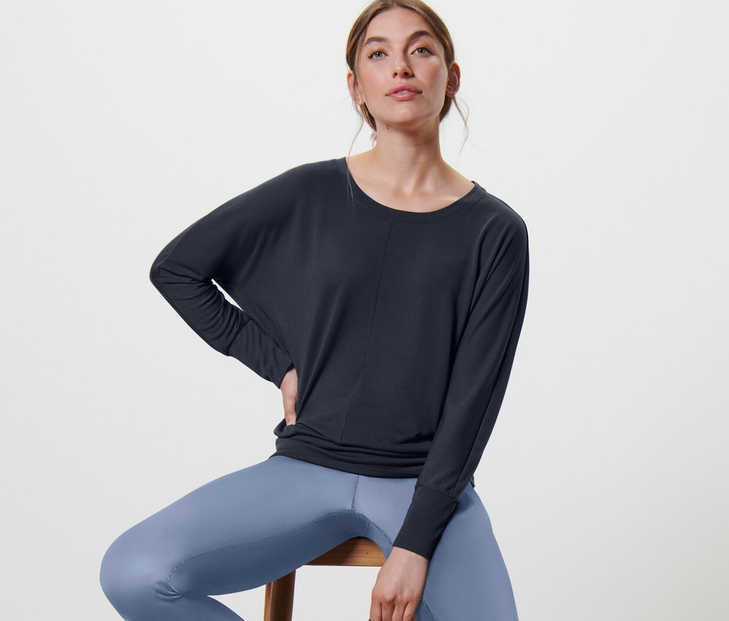 Kobieta siedzi na stołku, ubrana w granatową koszulkę do sportu i jogi.