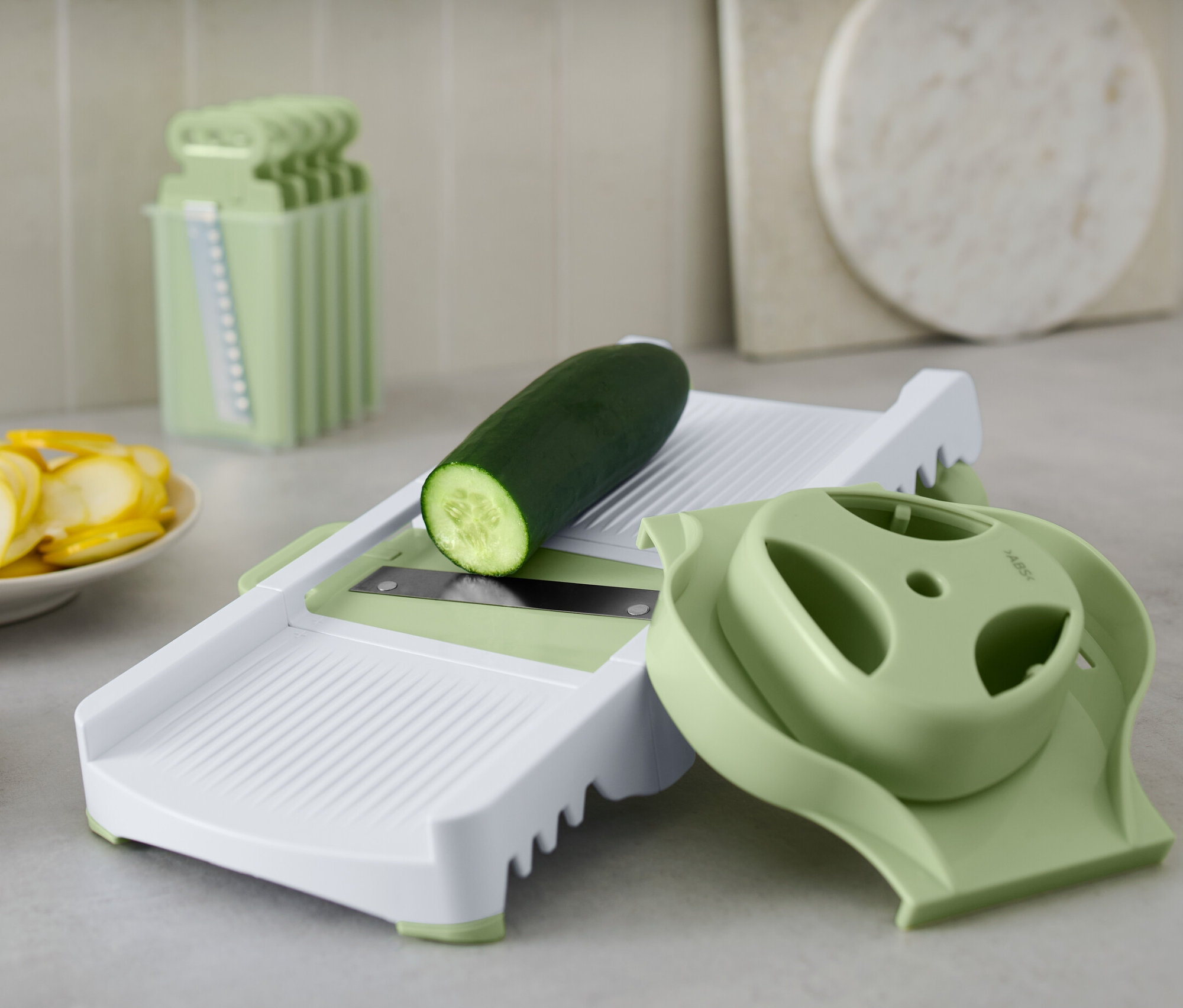 Ogórek leży na tarce wielofunkcyjnej. Obok leżą pokrojone ogórki i cukinia.