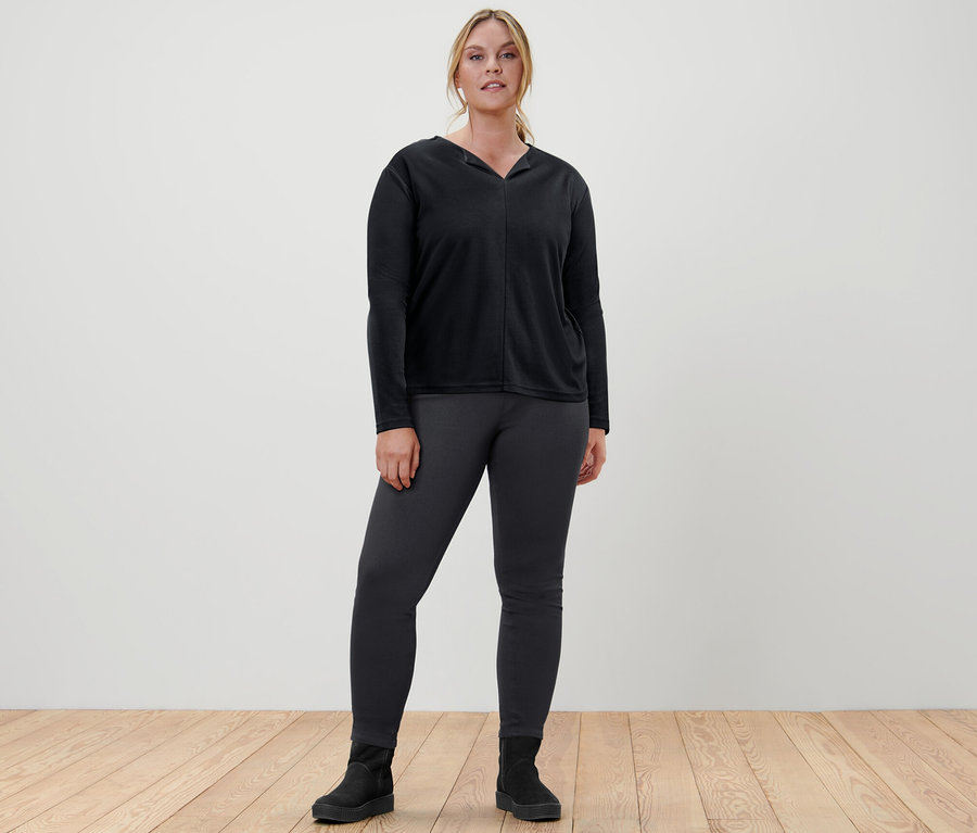 Kobieta stoi w czarnej bluzce i jegginsach.