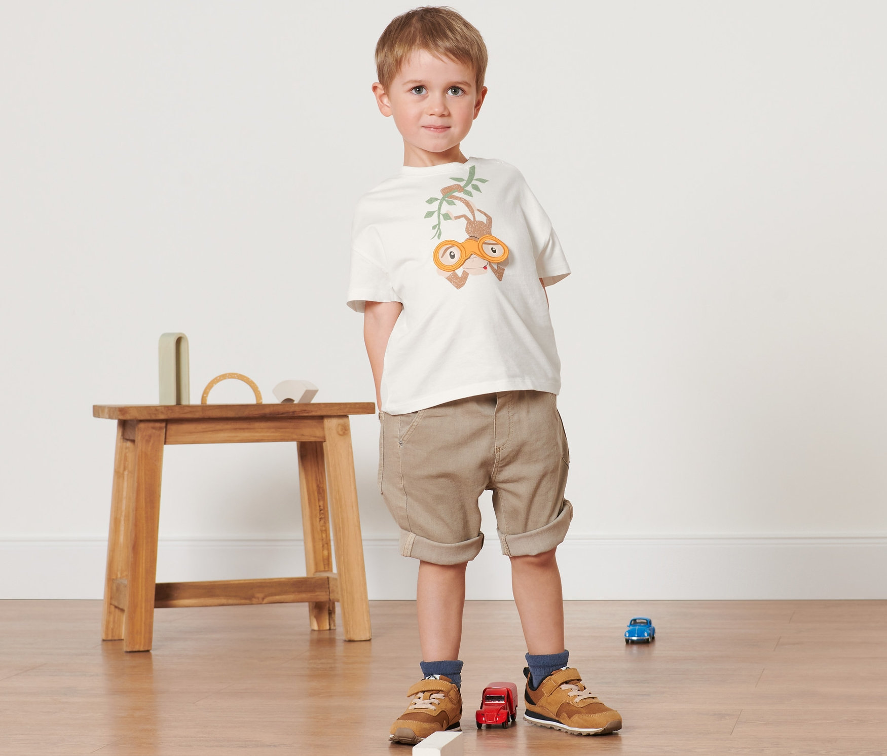 Chłopiec stoi na podłodze i ma na sobie 2 koszulki dziecięce.