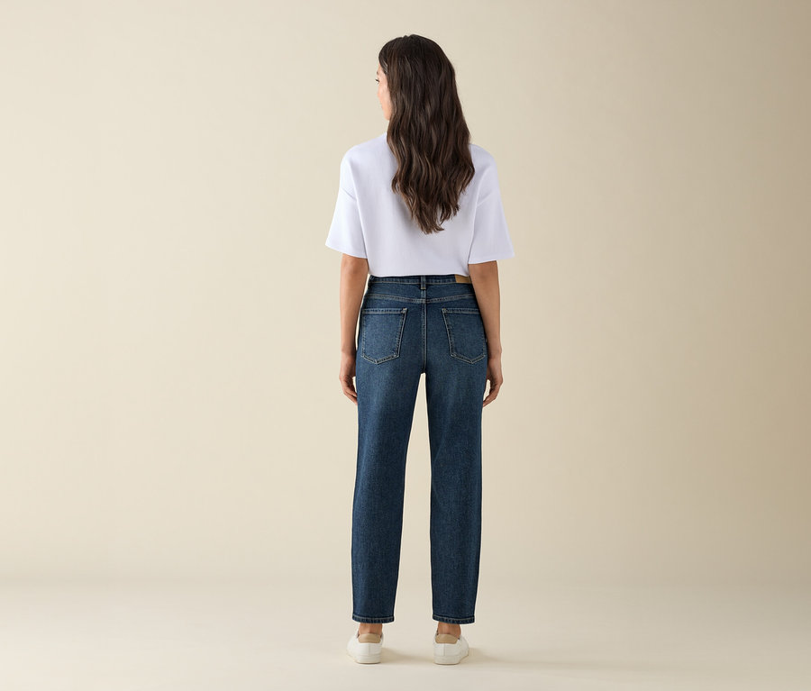 Kobieta od tyłu ma na sobie dżinsy typu mom – fason „Nyla”, dark blue, biały T-shirt i tenisówki.
