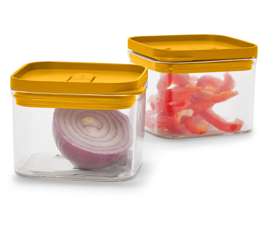 Dwa przezroczyste, kwadratowe pojemniki z musztardowożółtymi pokrywkami. W jednym znajduje się połówka czerwonej cebuli, w drugim pokrojona czerwona papryka.
