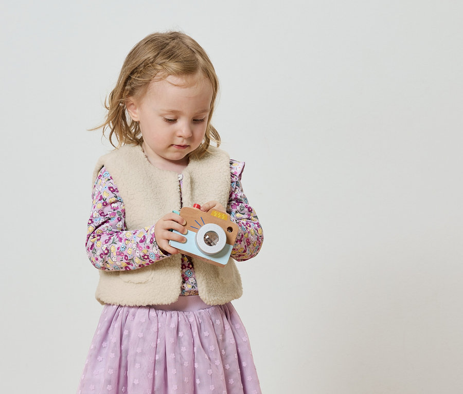 Mała dziewczynka z blond warkoczami trzyma zabawkę-aparat.