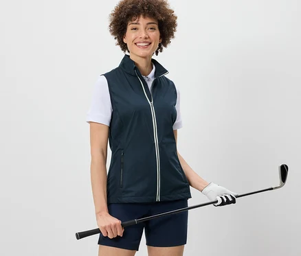 Kobieta ma na sobie kamizelkę softshellową i trzyma kij golfowy.