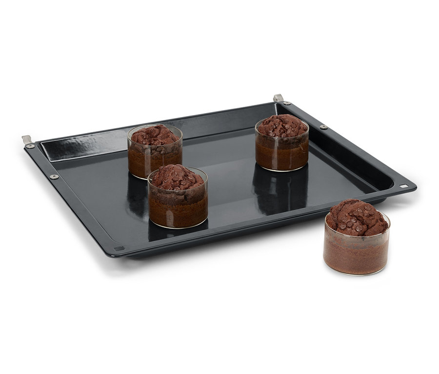 Cztery babeczki czekoladowe w szklankach na czarnej blasze do pieczenia.