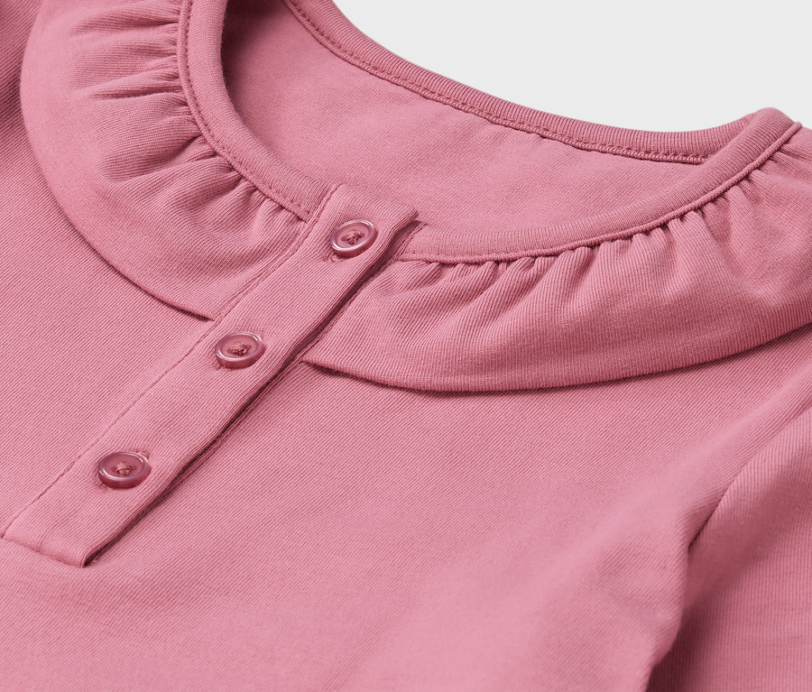 Szczegół różowej koszuli z kołnierzykiem i guzikami.