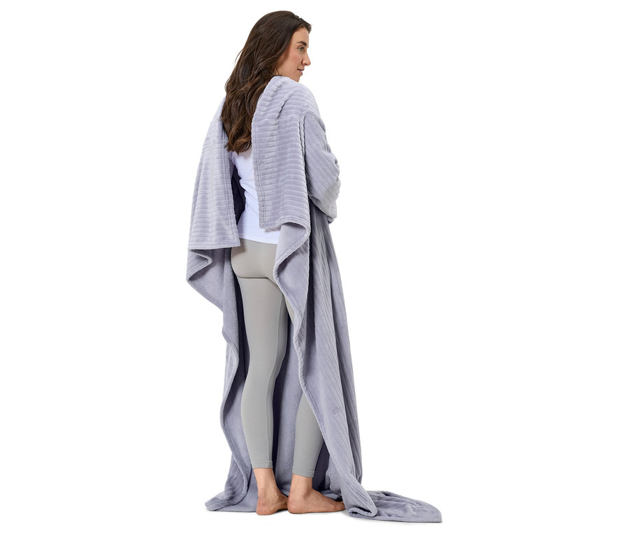 Kobieta stoi tyłem do kamery, owinięta szarym kocem.