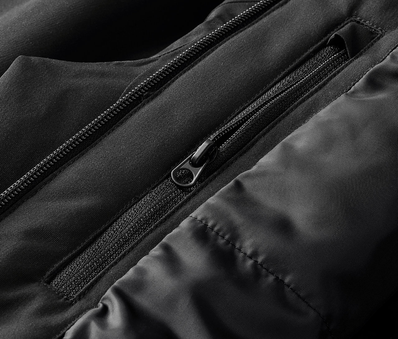 Zbliżenie na czarną kurtkę z widocznymi zamkami błyskawicznymi i pikowaniem.