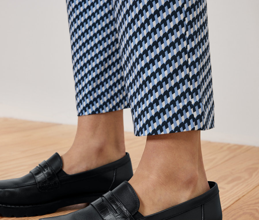 Nogi osoby w niebiesko-białych spodniach w kratę i czarnych skórzanych mokasynach na drewnianej podłodze.