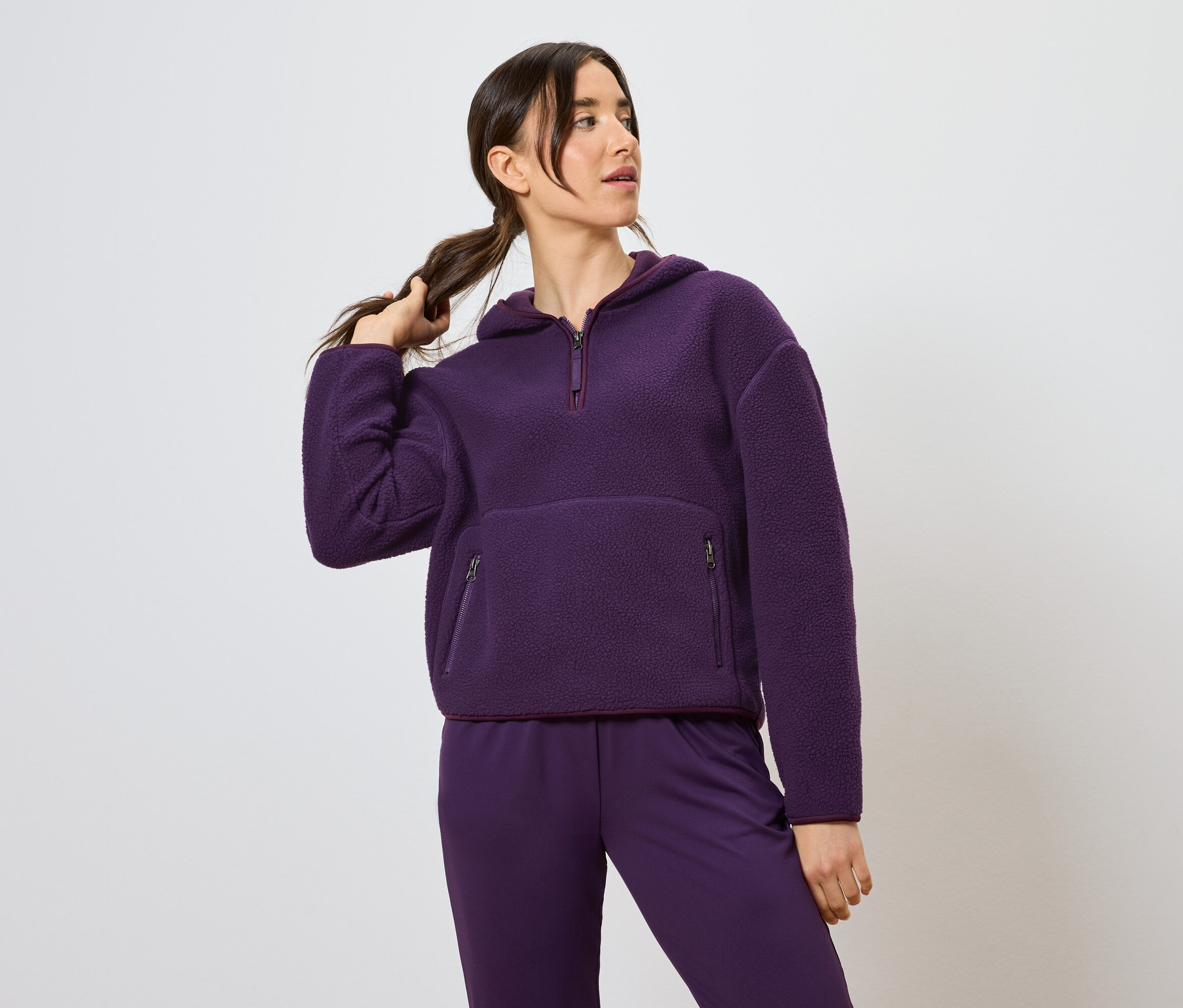 Kobieta trzyma kucyk, ubrana w fioletową bluzę z kapturem i spodnie.