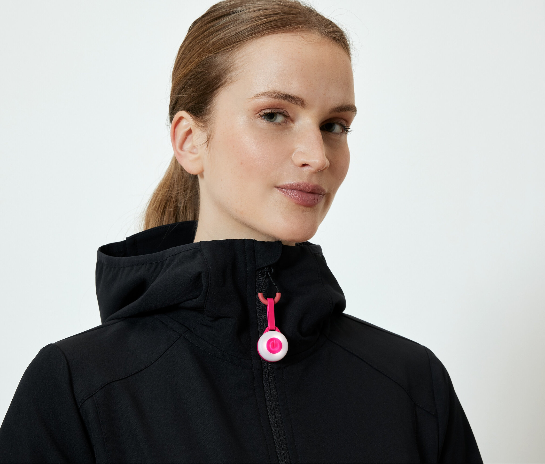 Kobieta ma na sobie czarną kurtkę z kapturem i różowym zamkiem błyskawicznym.