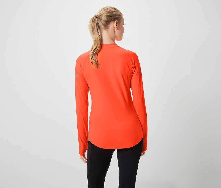 Widok z tyłu kobiety z blond włosami związanymi w kucyk, ubranej w pomarańczową bluzę sportową z długim rękawem i czarne legginsy.