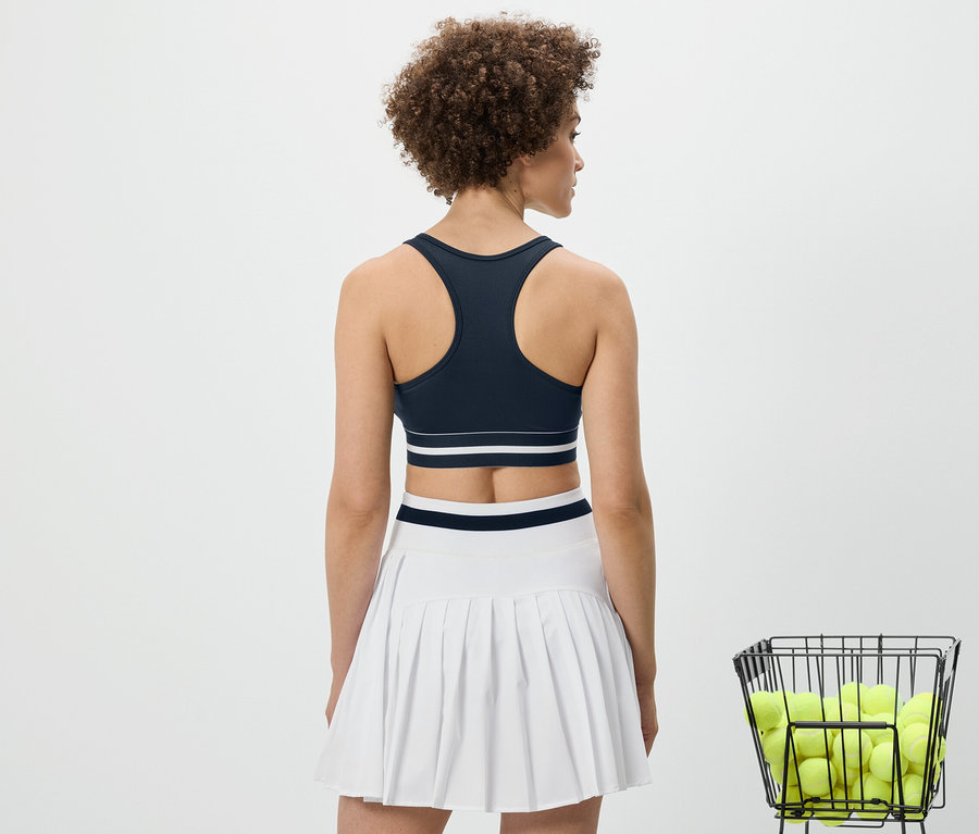 Widok z tyłu kobiety w niebieskiej sportowej braletce „Crop Top” i białej spódnicy.