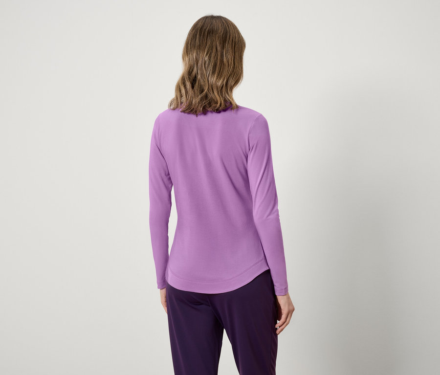 Widok z tyłu kobiety z falowanymi włosami w lawendowej bluzce z długim rękawem i fioletowych spodniach.