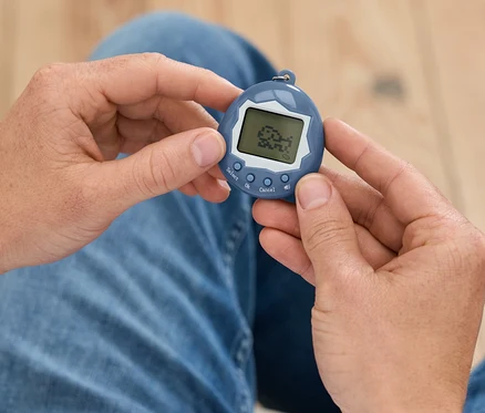 Mężczyzna trzyma w dłoniach niebieskie Tamagotchi.