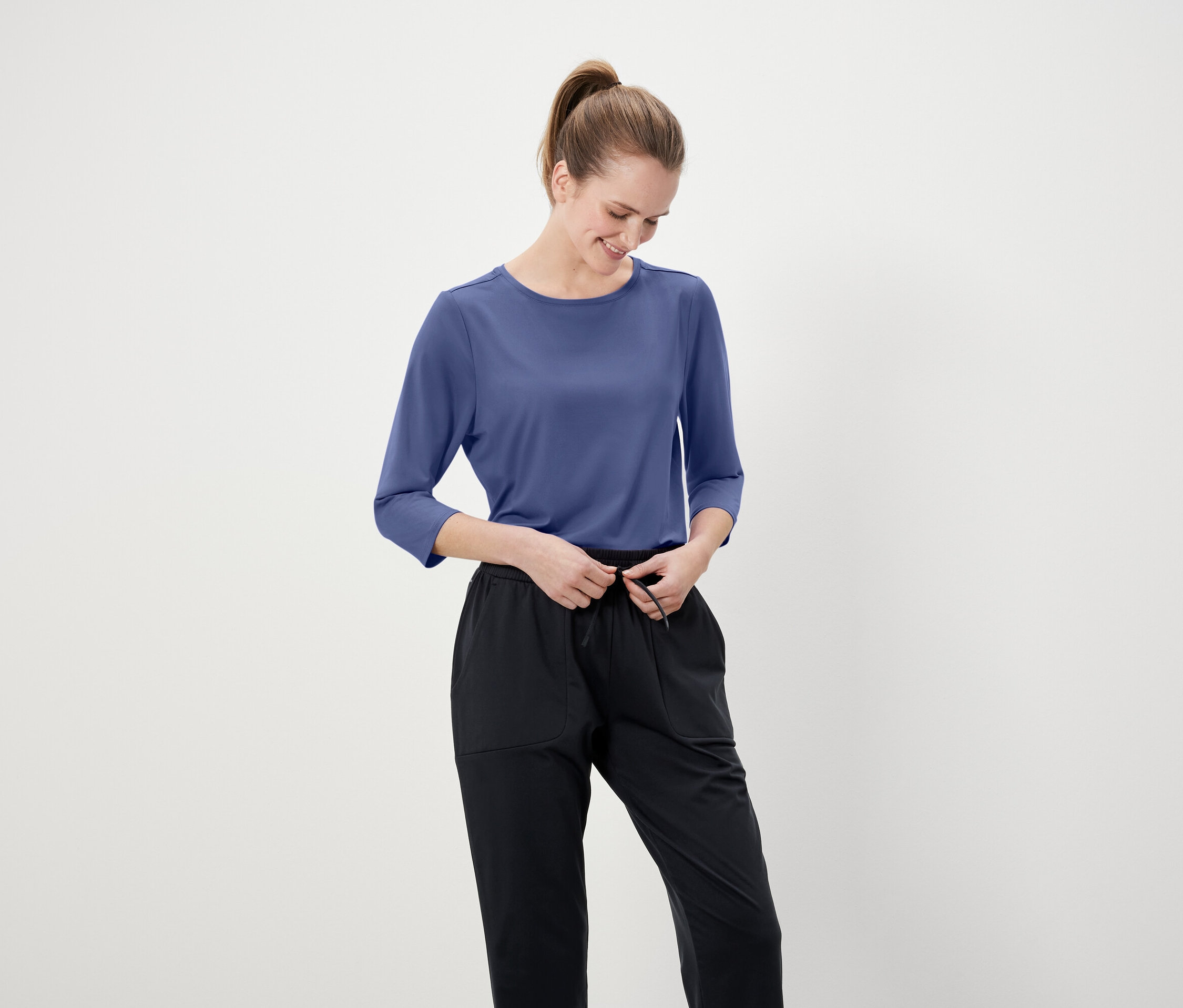 Kobieta poprawia czarne spodnie w niebieskiej koszulce z rękawem trzy czwarte.
