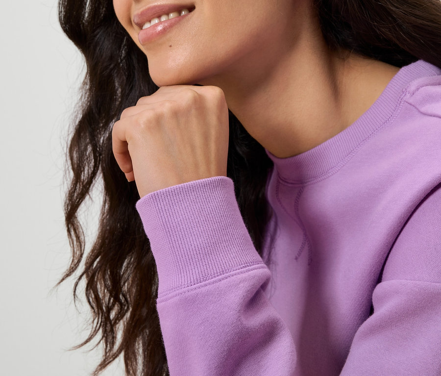 Zbliżenie na kobietę z falowanymi, ciemnymi włosami, która podpiera brodę ręką. Ma na sobie jasno fioletową bluzę.