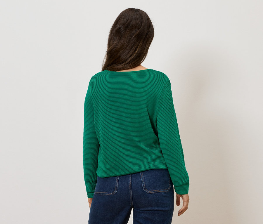 Kobieta stoi tyłem, ubrana w zielony sweter i dżinsy.