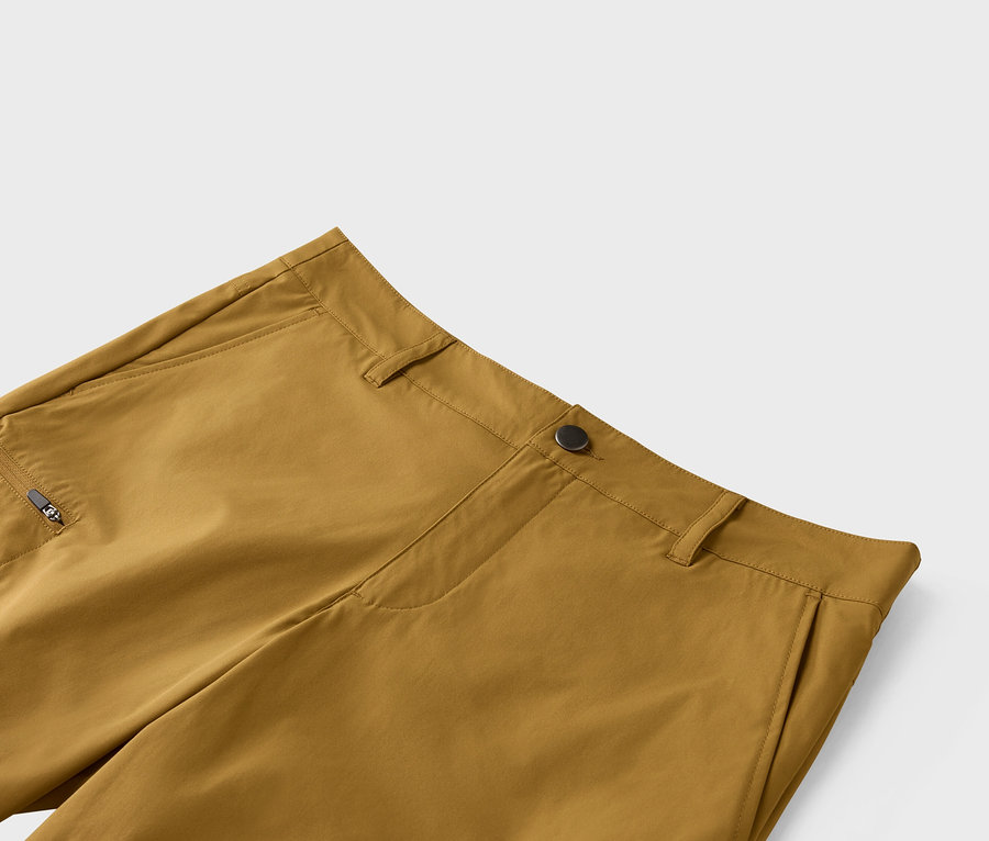 Zbliżenie na ochrowe spodnie z zapięciem na guzik i kieszenią na zamek błyskawiczny.