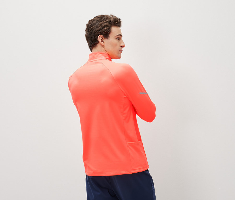 Mężczyzna w koralowej koszulce sportowej z długim rękawem i granatowych szortach sportowych.