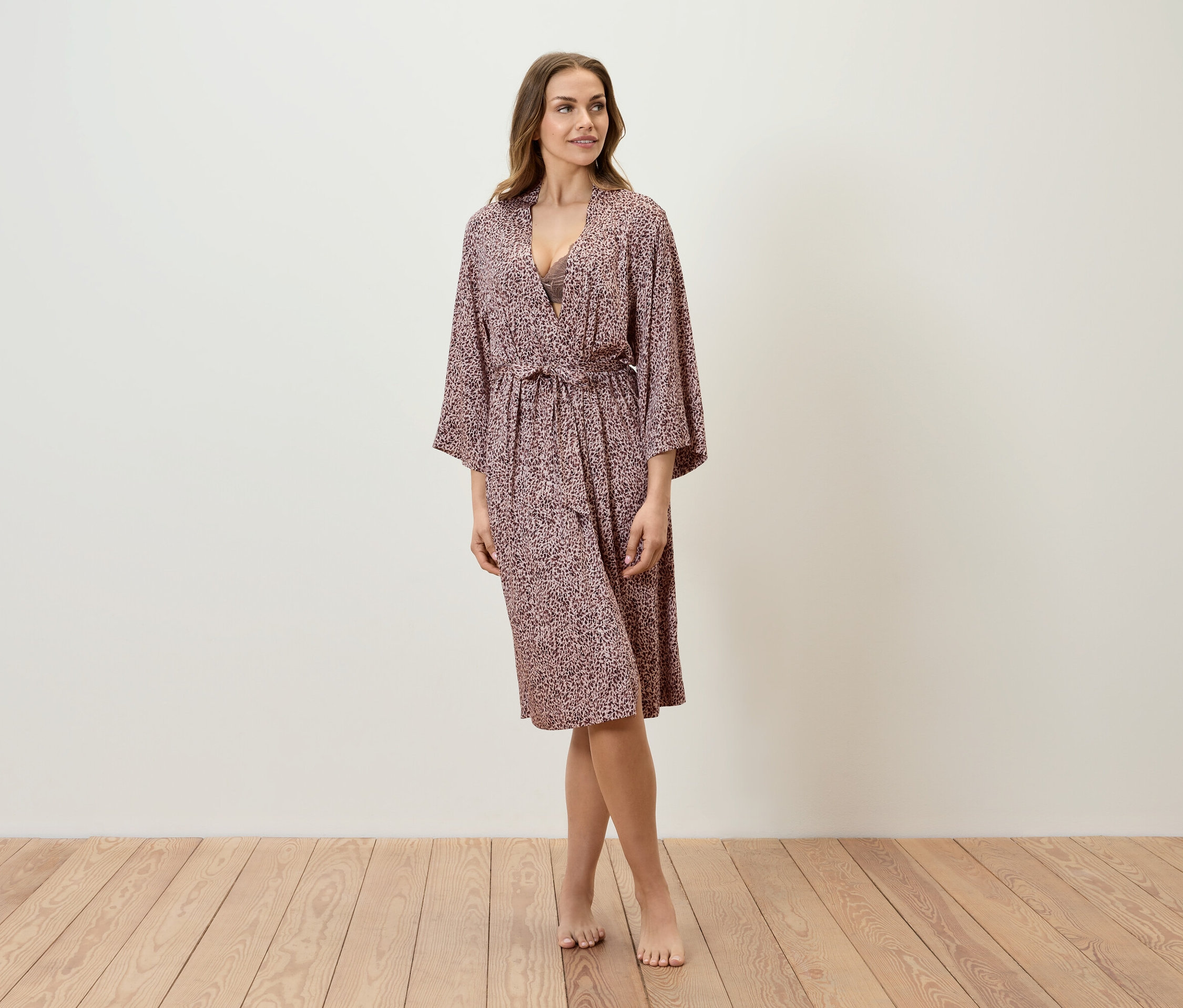 Kobieta stoi na drewnianej podłodze i ma na sobie wzorzysty szlafrok.