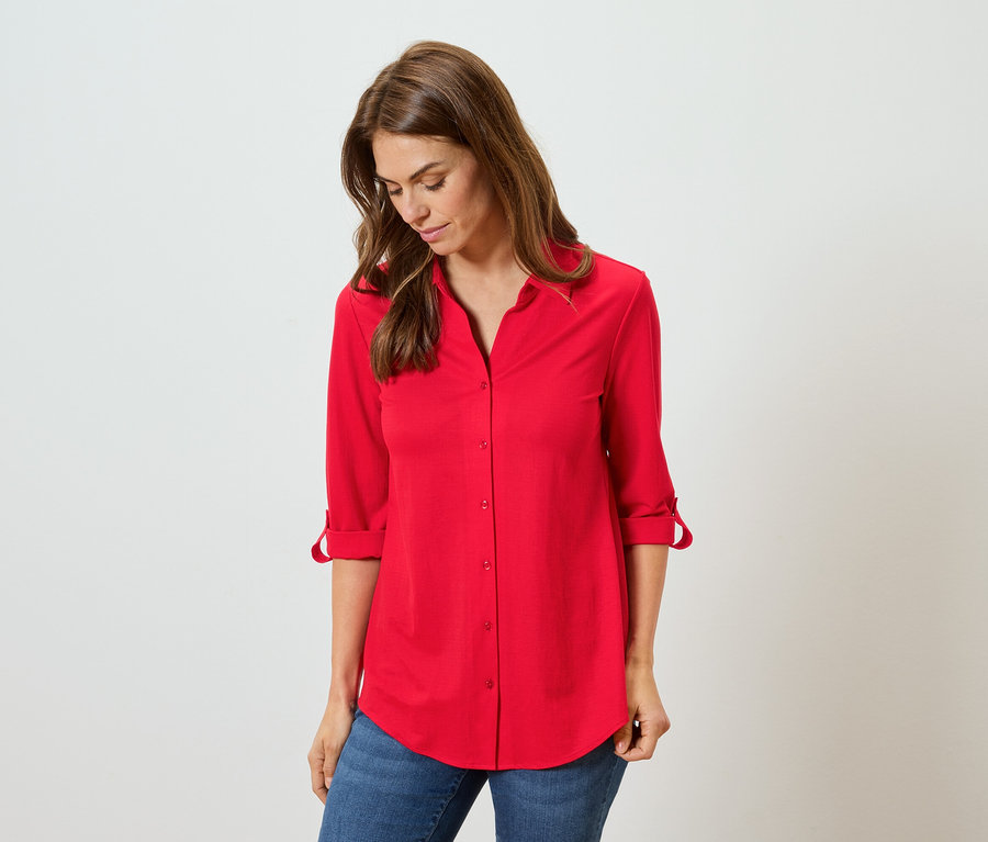 Kobieta ma na sobie czerwoną koszulę i niebieskie dżinsy.
