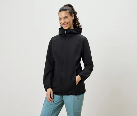 Uśmiechnięta kobieta z włosami związanymi w kucyk ma na sobie czarną kurtkę softshell i niebieskie spodnie.