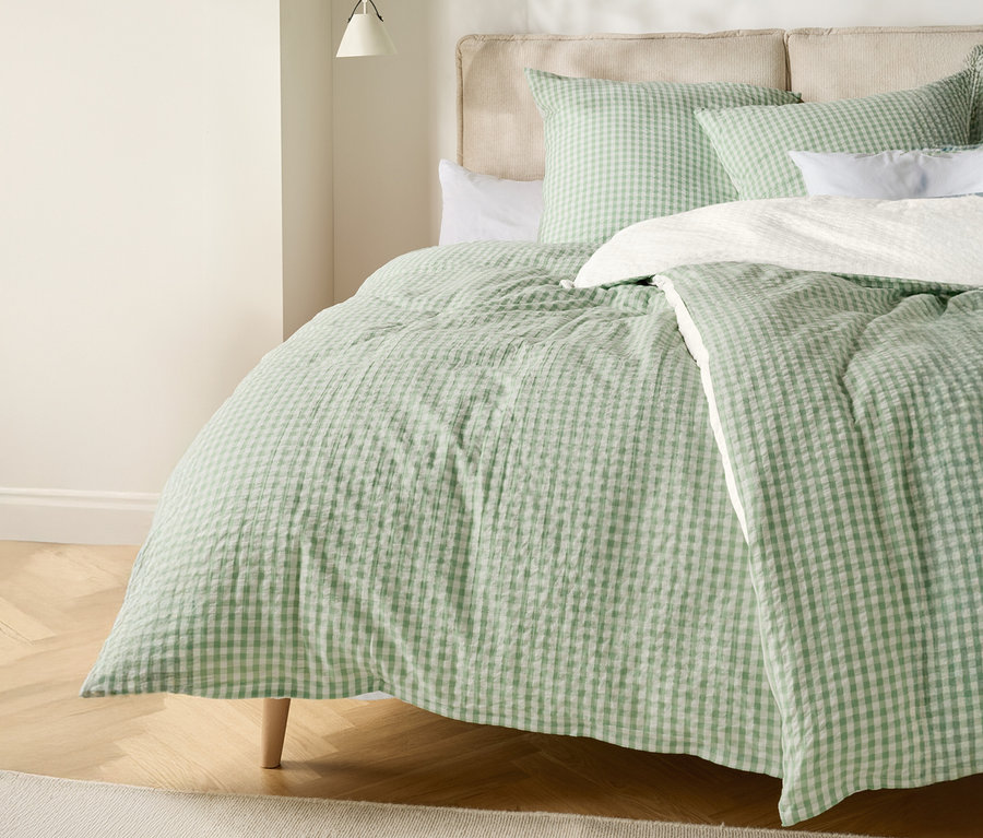 Łóżko z jasnozielono-białą kołdrą w kratę i pasującymi poduszkami.