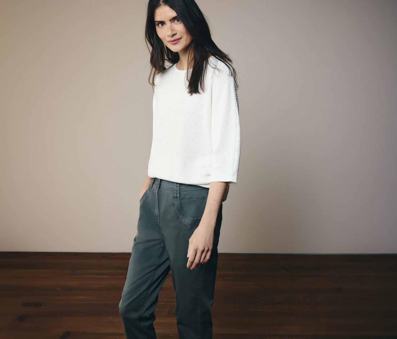 Kobieta w białej bluzce i spodniach CECIL „Scarlett” w kolorze ciemnej zieleni pozuje na jasnym tle.