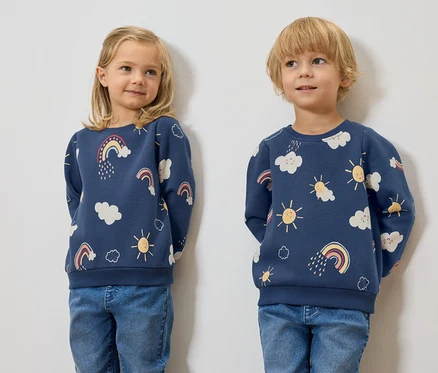 Dwoje dzieci stoi obok siebie, ubrani w granatowe bluzy dziecięce z ocieplanym wnętrzem, z nadrukowanymi chmurami, słońcami i tęczami.