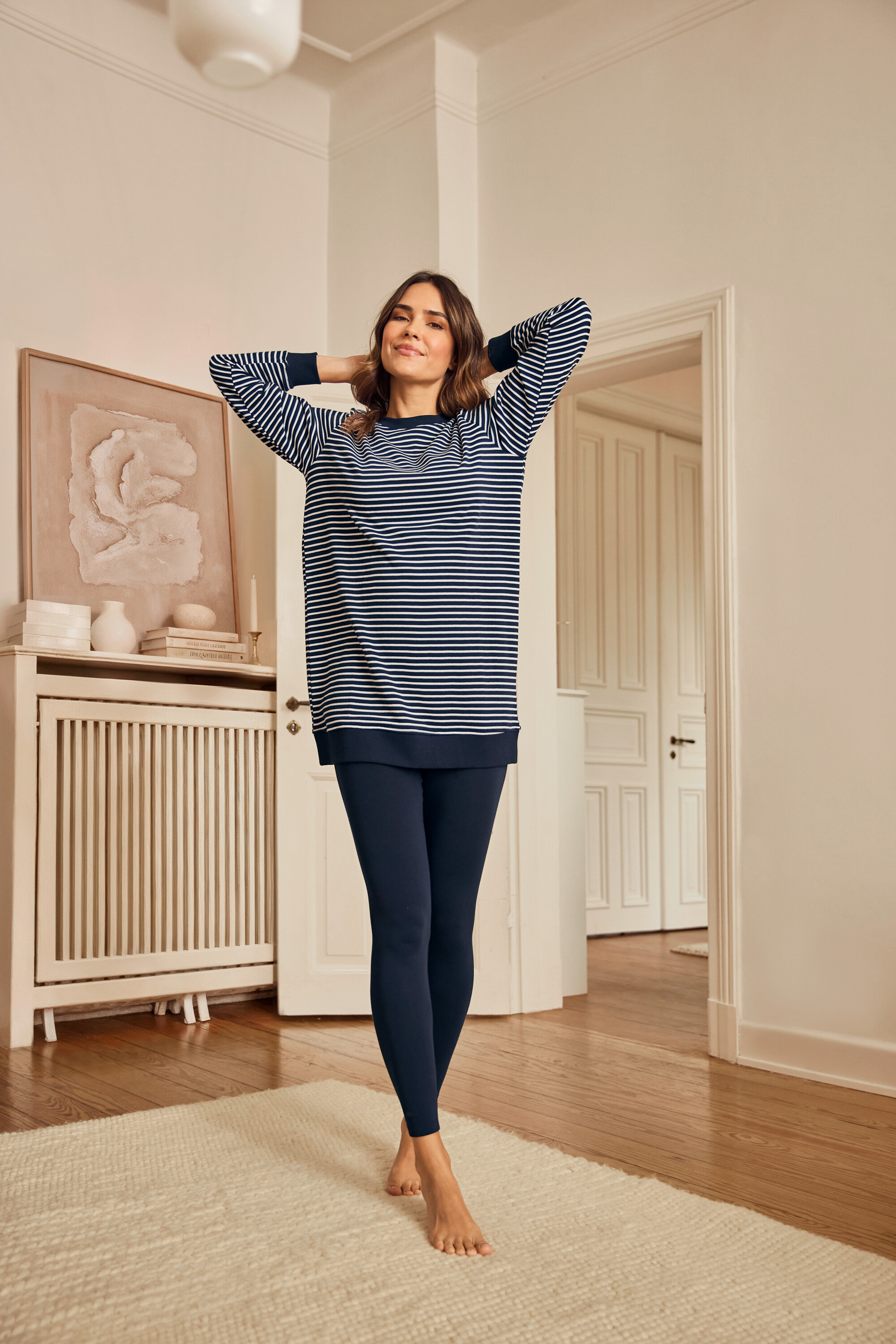 Kobieta w piżamie z legginsami stoi boso na dywanie.