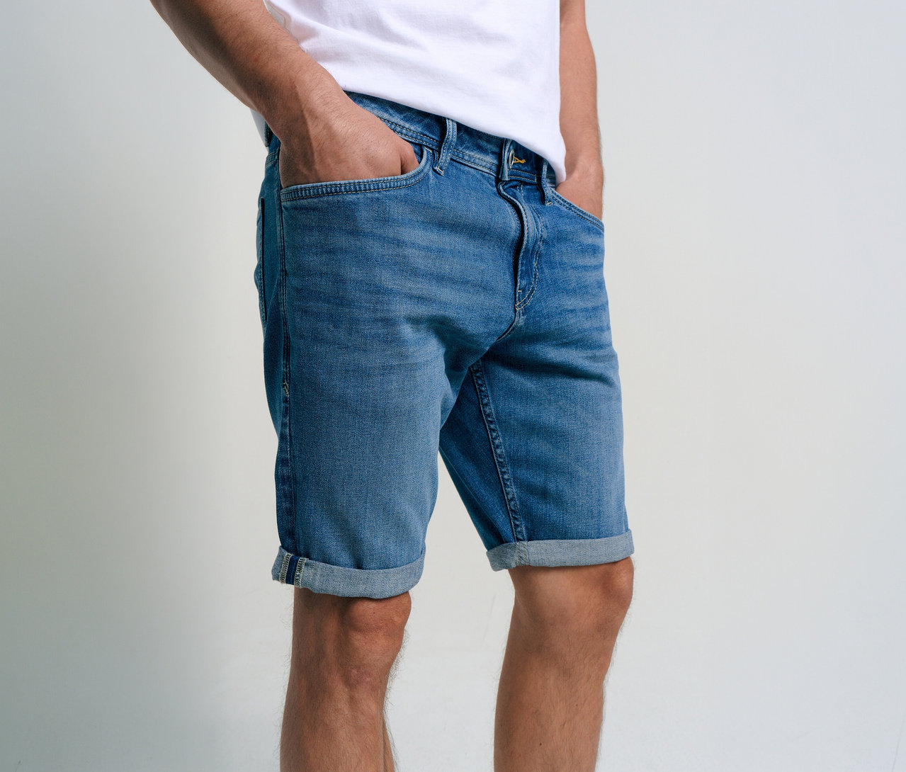 Mężczyzna w szortach dżinsowych Tom Tailor TTJOSH REGULAR SLIM, mid stone bright blue denim, z rękami w kieszeniach.