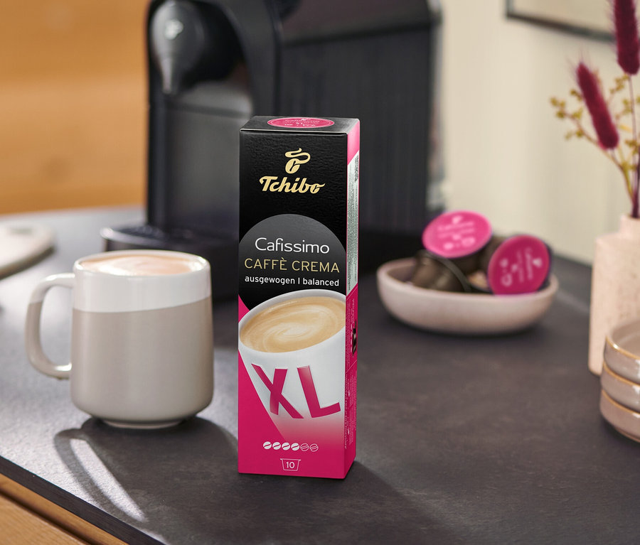 Ekspres do kawy stoi obok opakowania Caffè Crema Wake Up XL – 80 kapsułek i filiżanki na blacie kuchennym.