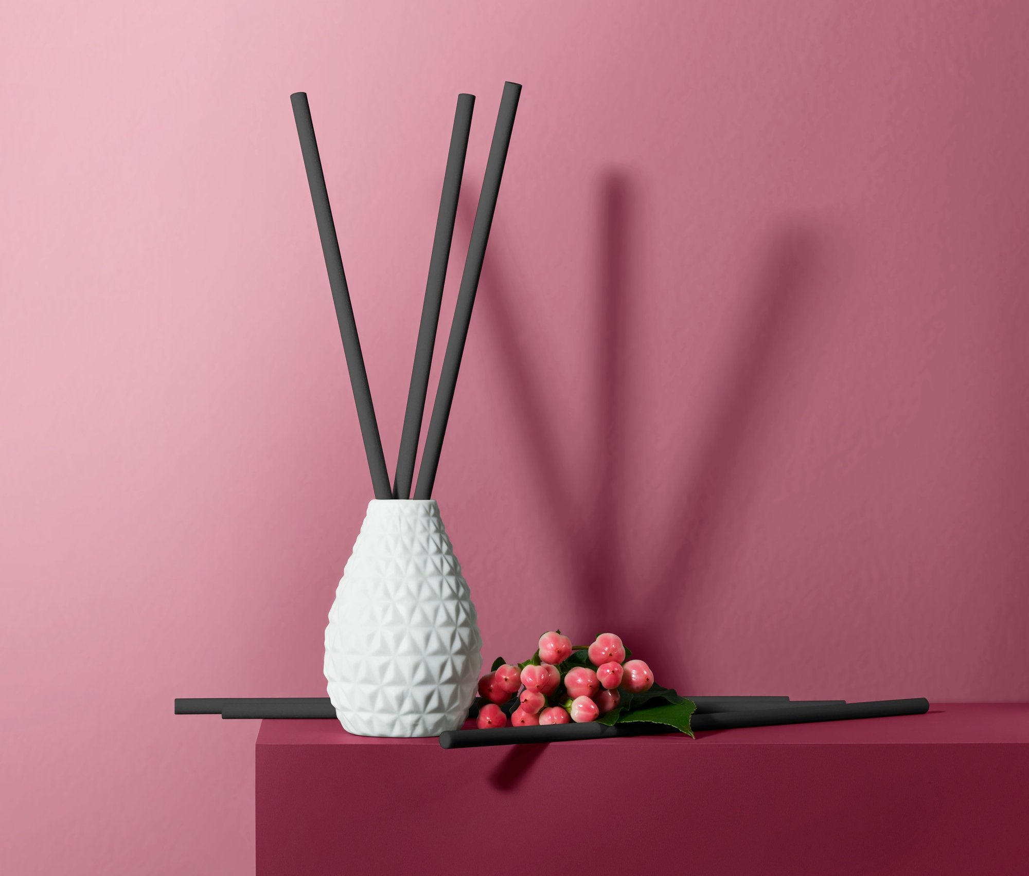 Zestaw do aromatyzowania powietrza »Drzewo cedrowe« z białą wazą i czarnymi patyczkami na bordowym cokole na różowym tle.