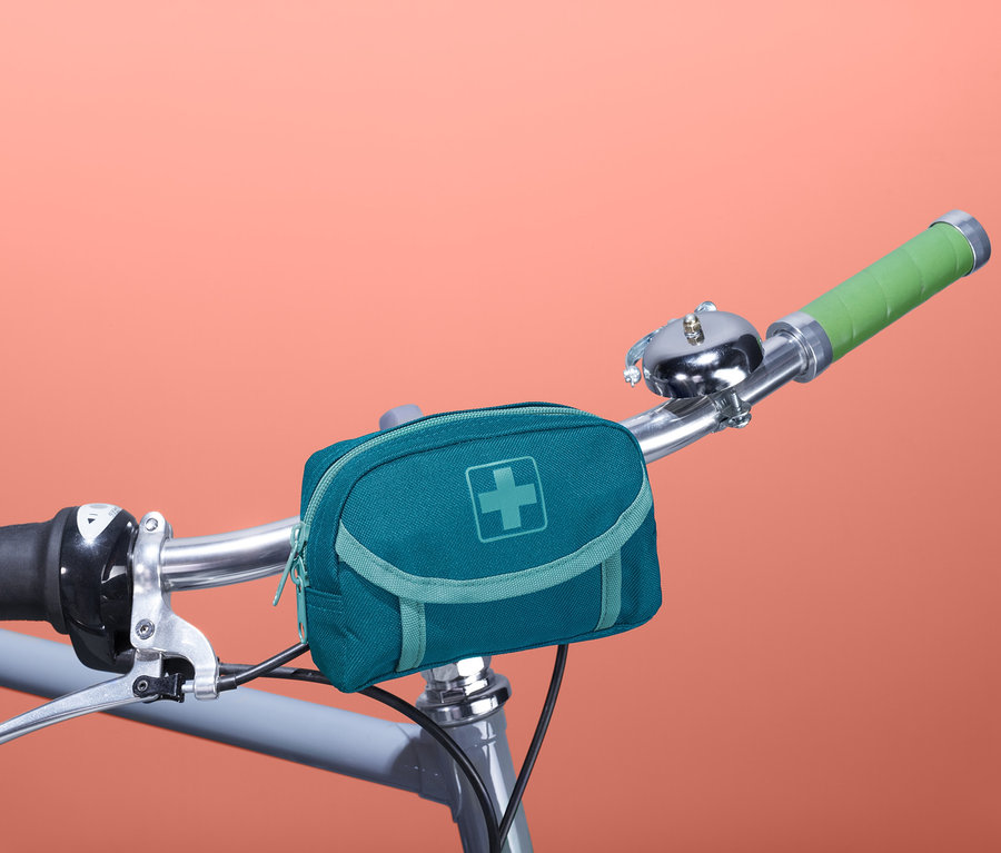 Na kierownicy roweru przymocowana jest niebiesko-zielona apteczka pierwszej pomocy.