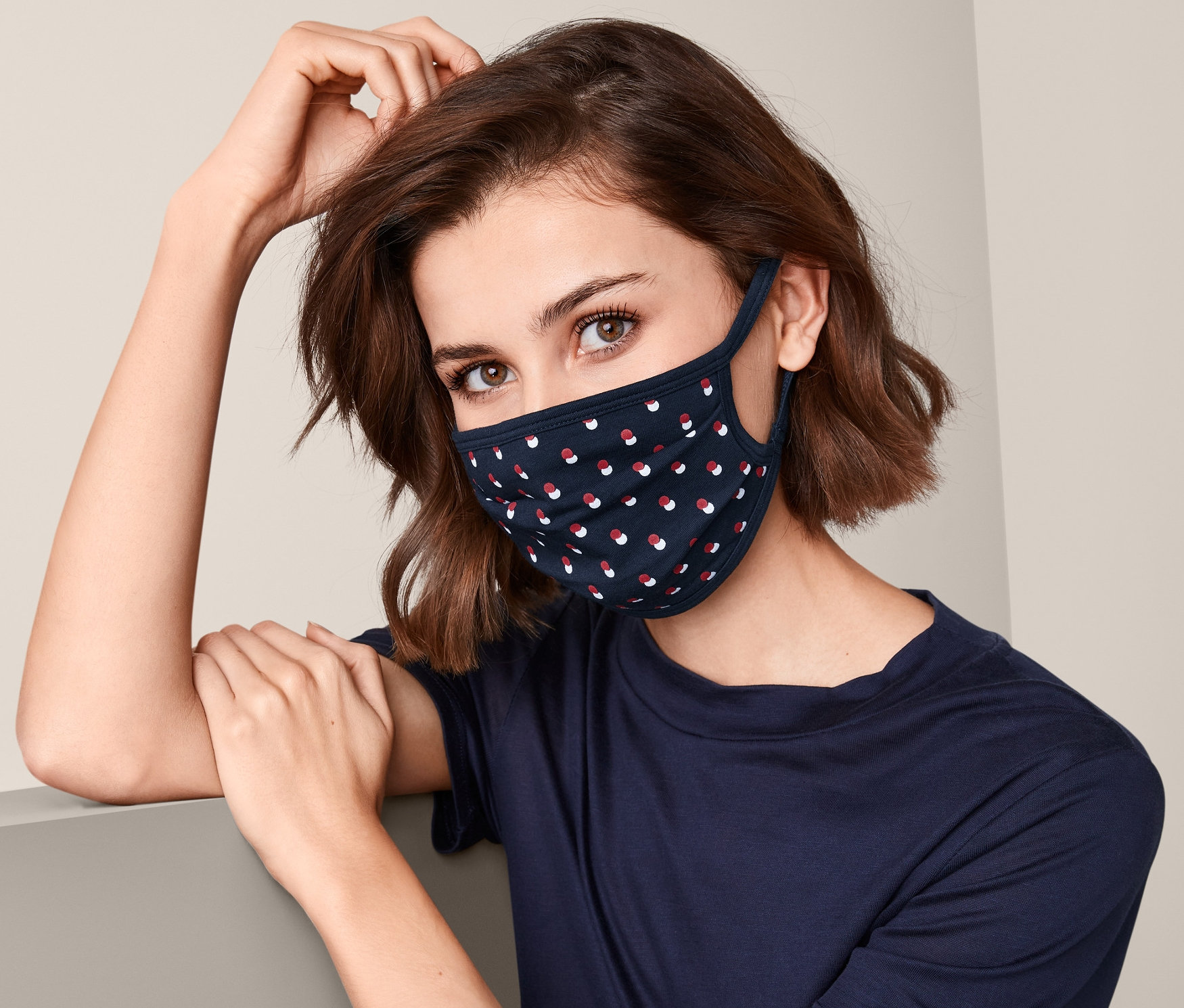 Kobieta nosi granatową maseczkę ochronną, 3 sztuki, w czerwone i białe kropki.
