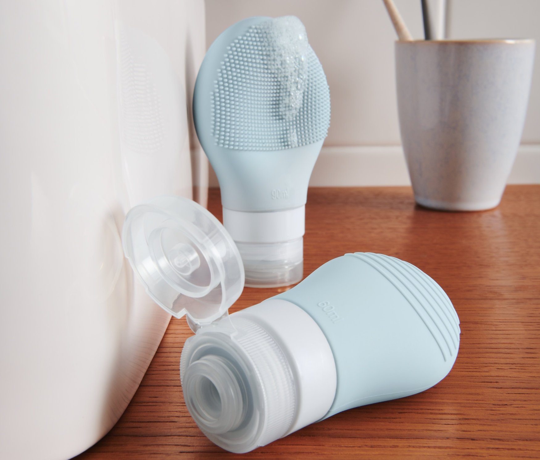 Dwie niebieskie buteleczki na szampon stoją na drewnianej półce obok umywalki.