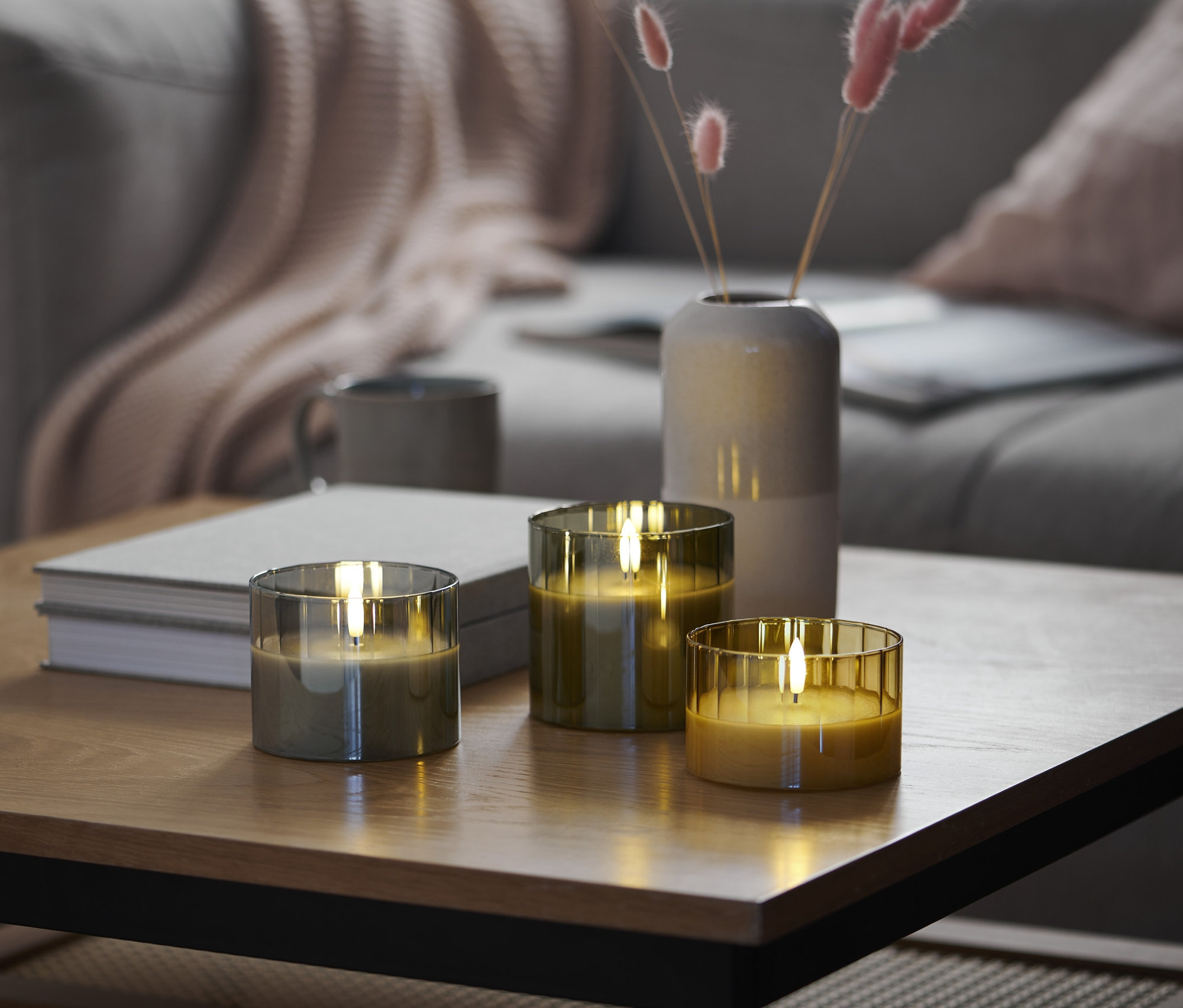 Trzy świece LED z prawdziwego wosku w szklanych pojemnikach stoją na stole w salonie.