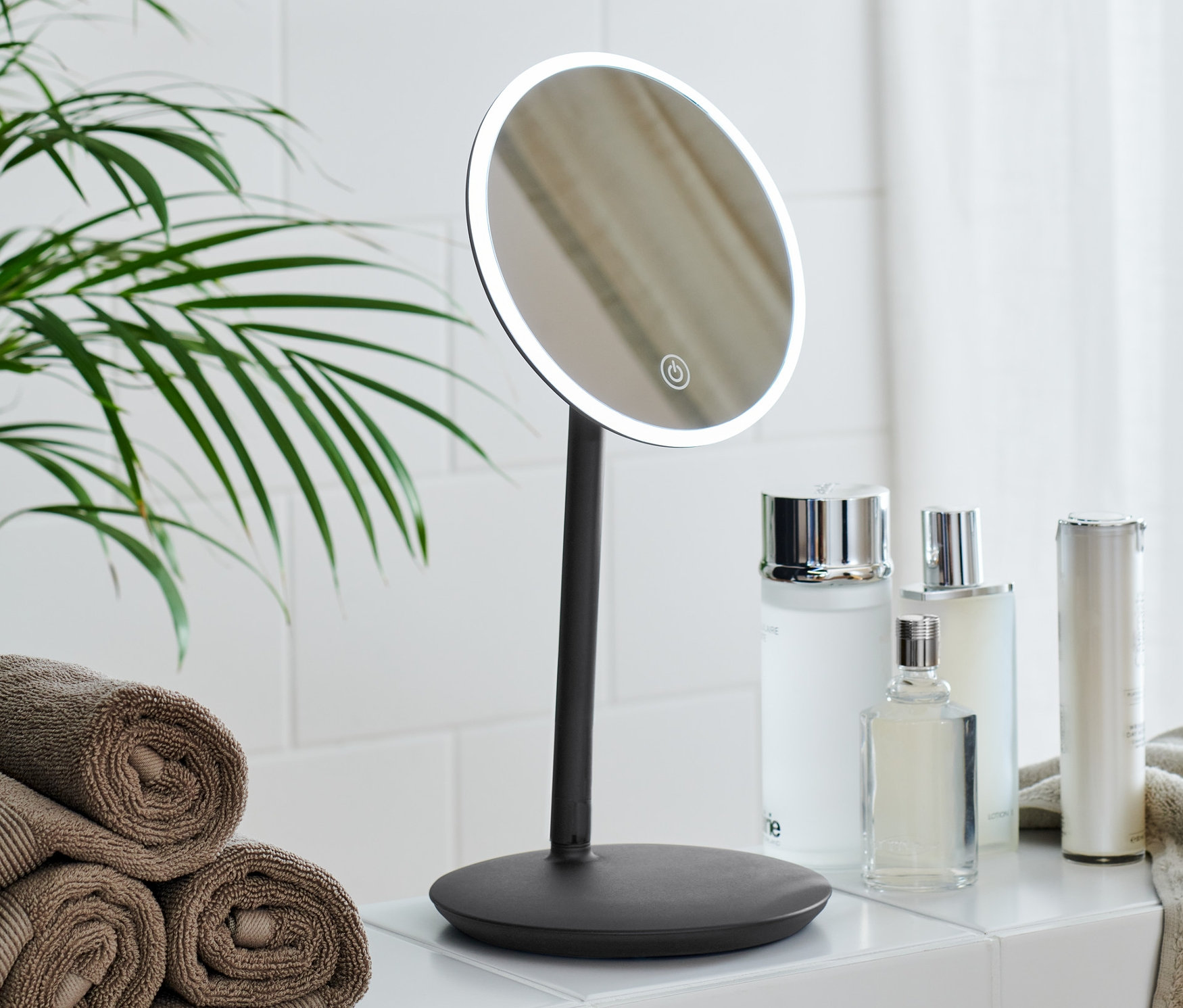 Łazienka z lusterkiem kosmetycznym z podświetleniem LED, kosmetykami i stosem ręczników.