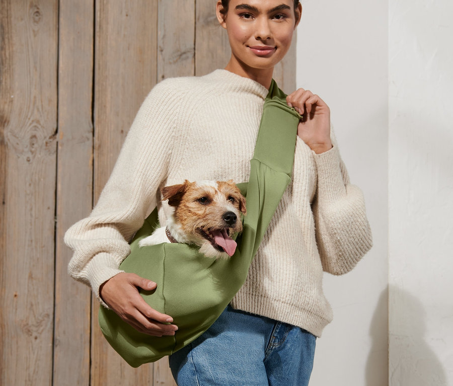 Kobieta niesie psa w zielonej torbie do transportu zwierząt.