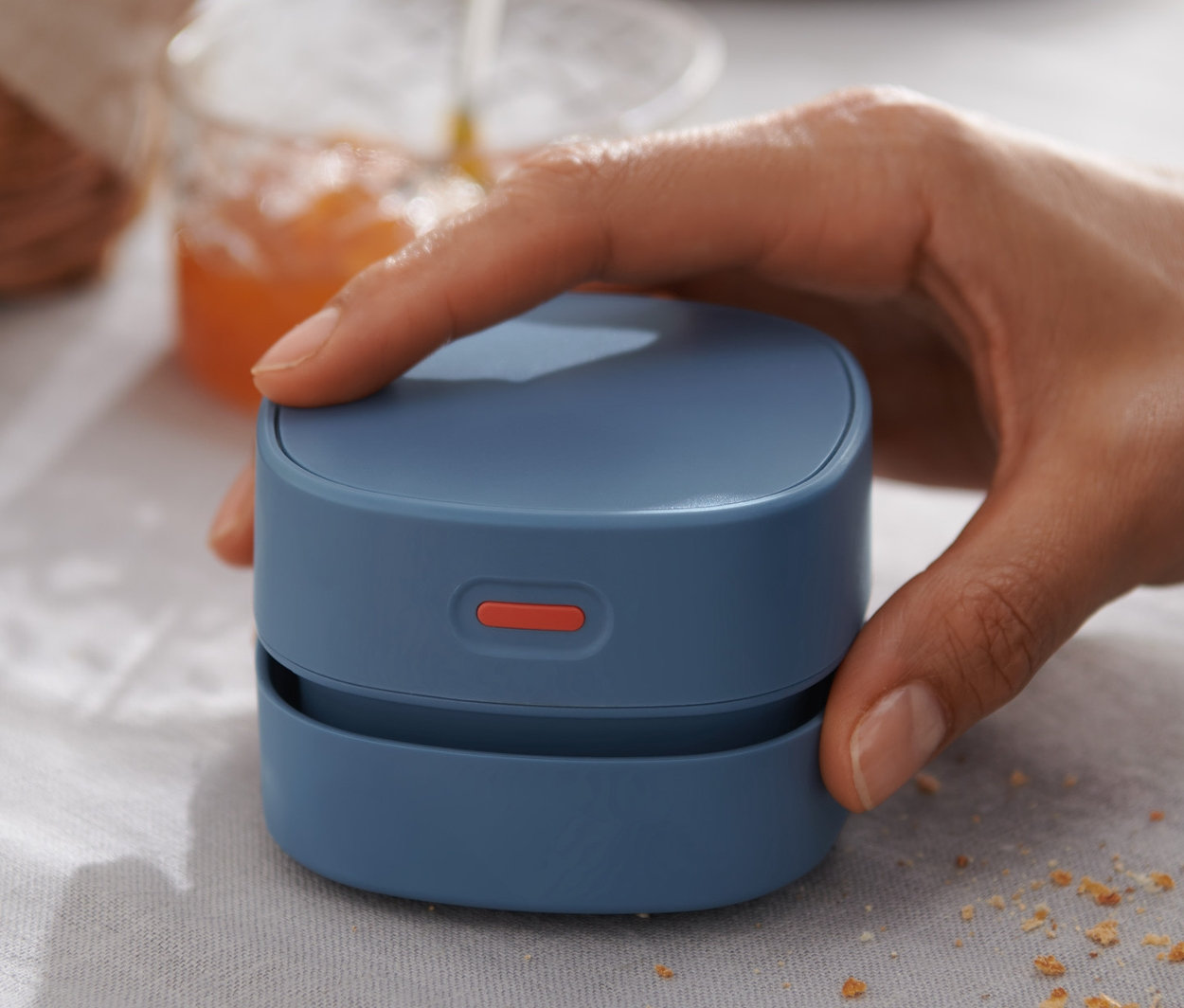 Ręka trzyma niebieski miniodkurzacz stołowy na stole z okruchami.