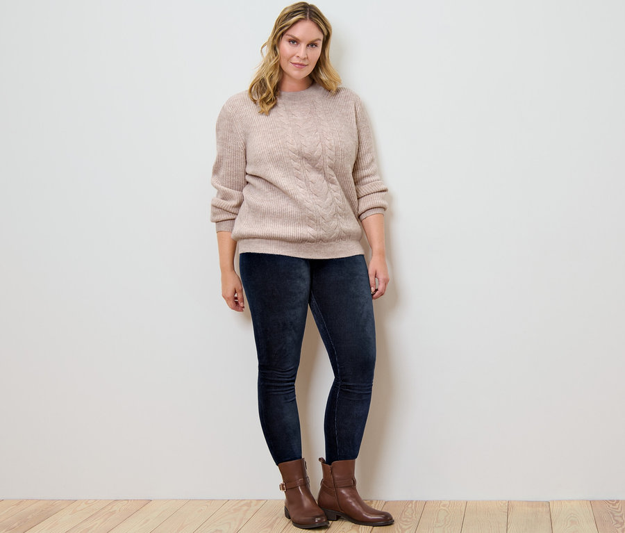 Kobieta pozuje w swetrze o grubym splocie z wzorem warkoczowym i sztruksowych legginsach.