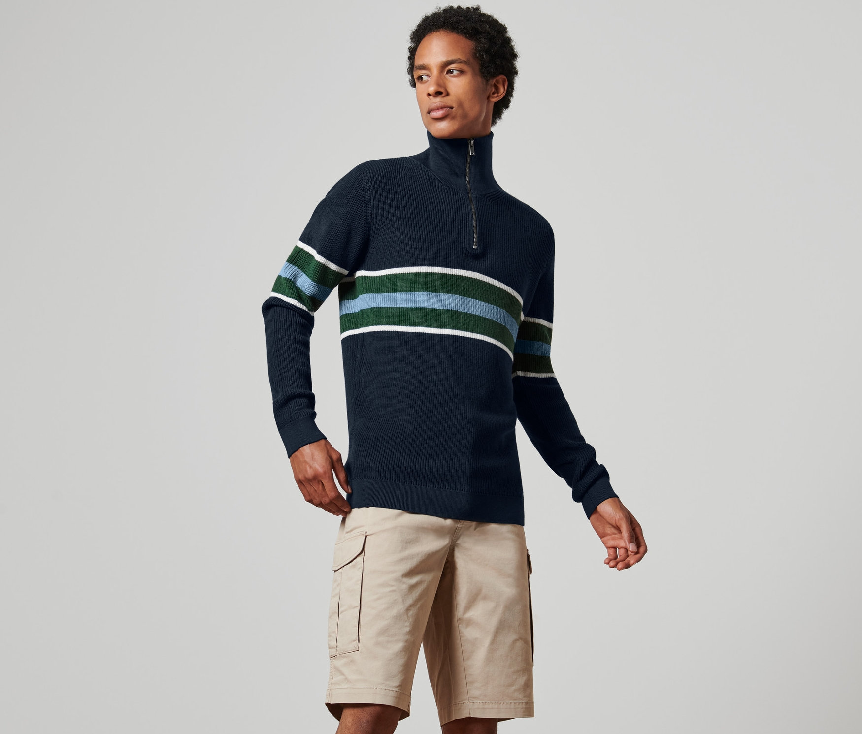 Mężczyzna ma na sobie granatowy sweter z golfem w paski i szorty khaki.