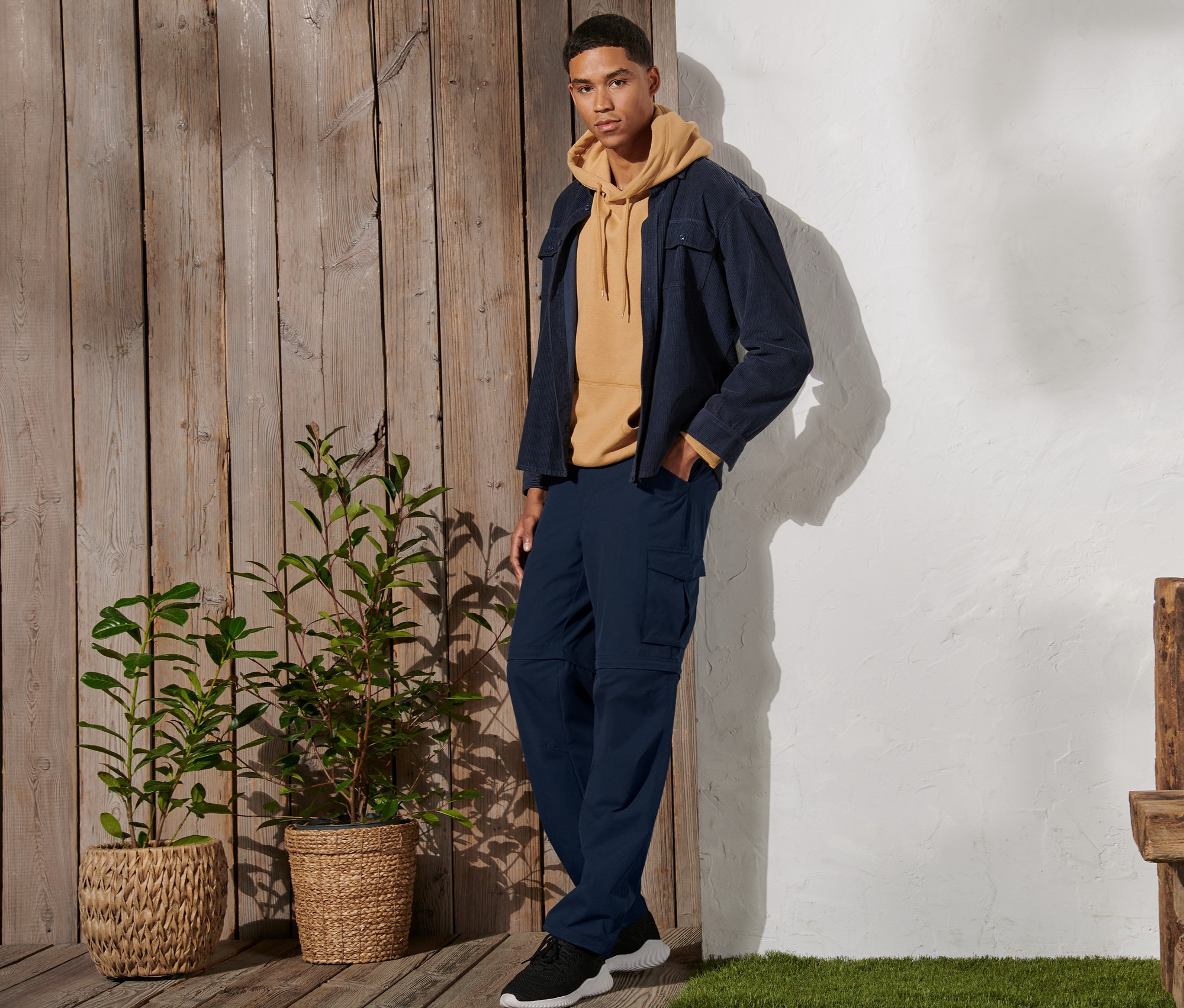 Mężczyzna stoi i ma na sobie granatowe spodnie funkcyjne 2 w 1, żółtą bluzę z kapturem i kurtkę.