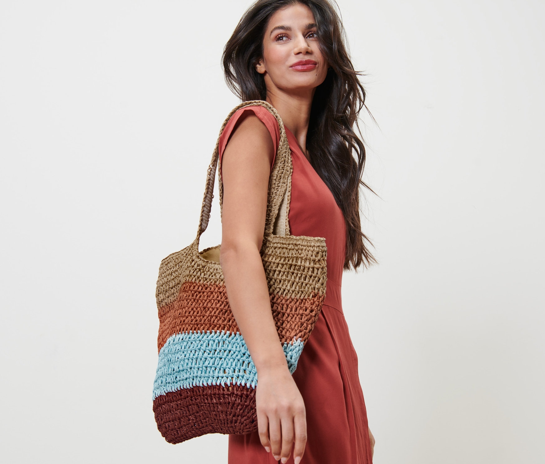 Kobieta w pomarańczowej sukience z plecioną torbą na ramieniu.