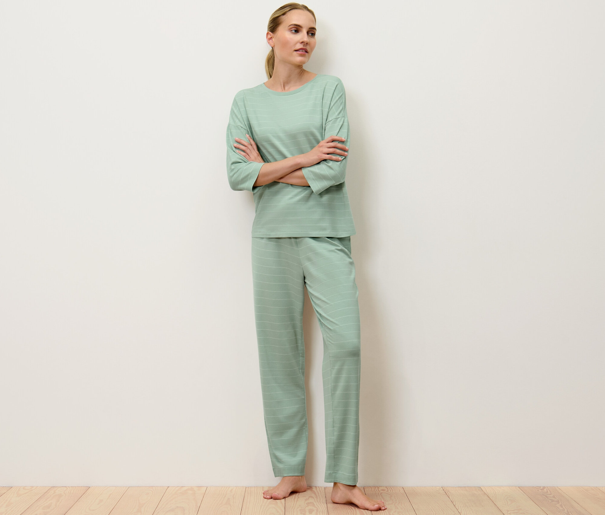 Kobieta stoi ze skrzyżowanymi ramionami, ubrana w jasnozieloną piżamę w paski.