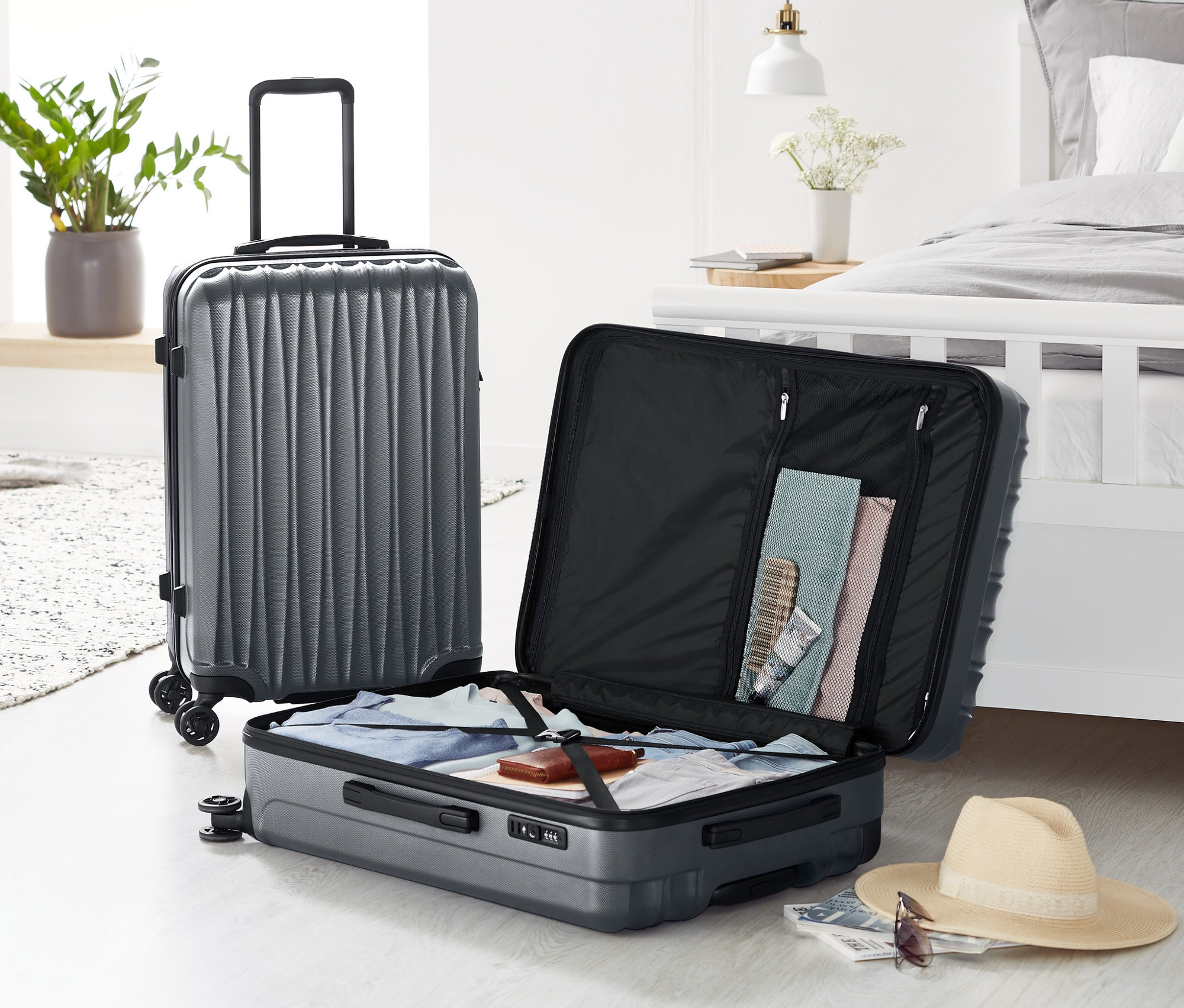 Dwa szare komplety twardych walizek, średnia i duża, stoją na podłodze, jeden otwarty.