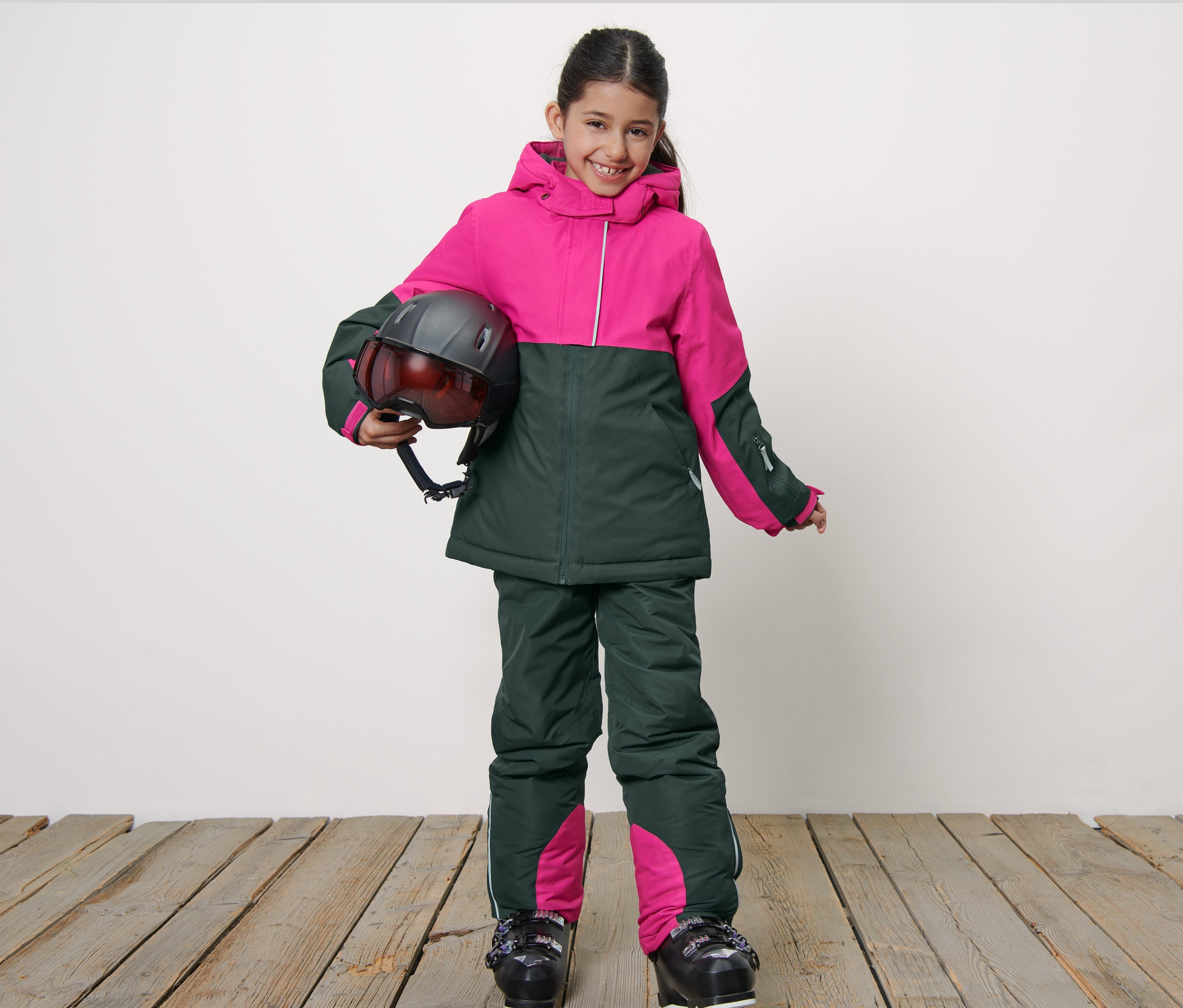 Uśmiechnięta dziewczyna w dziecięcej kurtce narciarskiej trzyma kask.