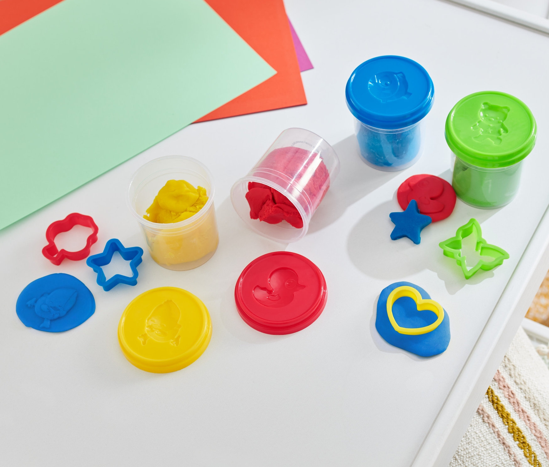 Zestaw ciastoliny na białym stole z kolorowymi papierami.